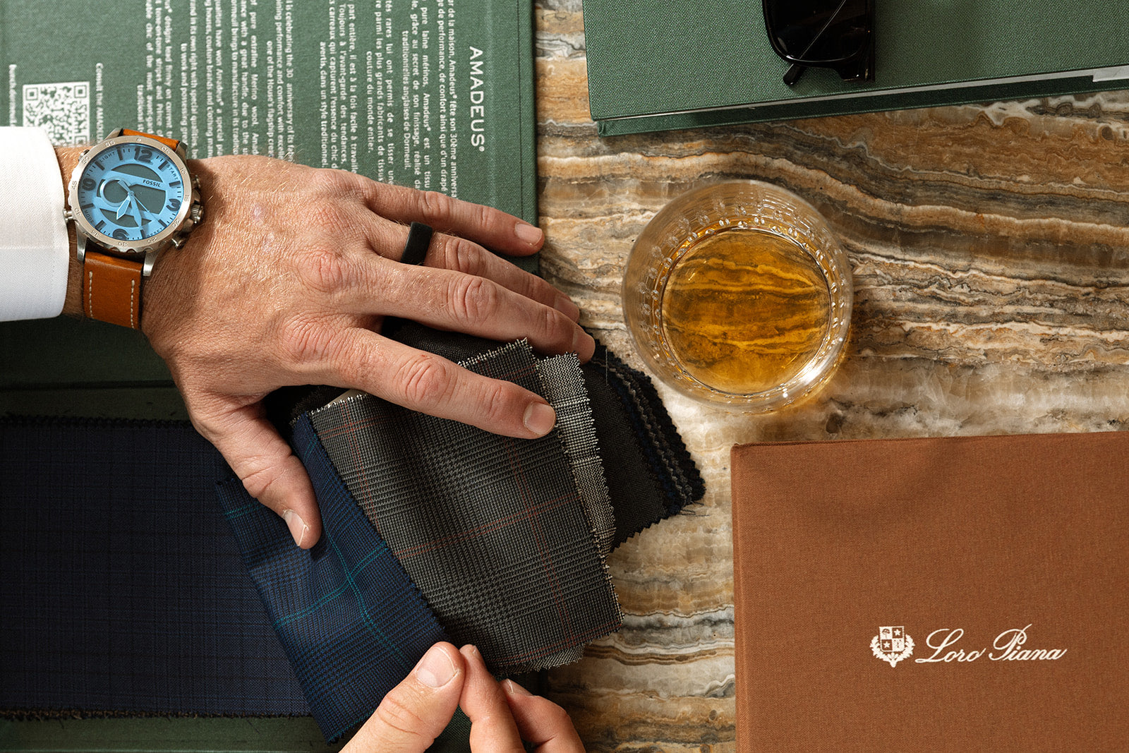 Hand resting on suiting swatches beside a Loro Piana fabric book