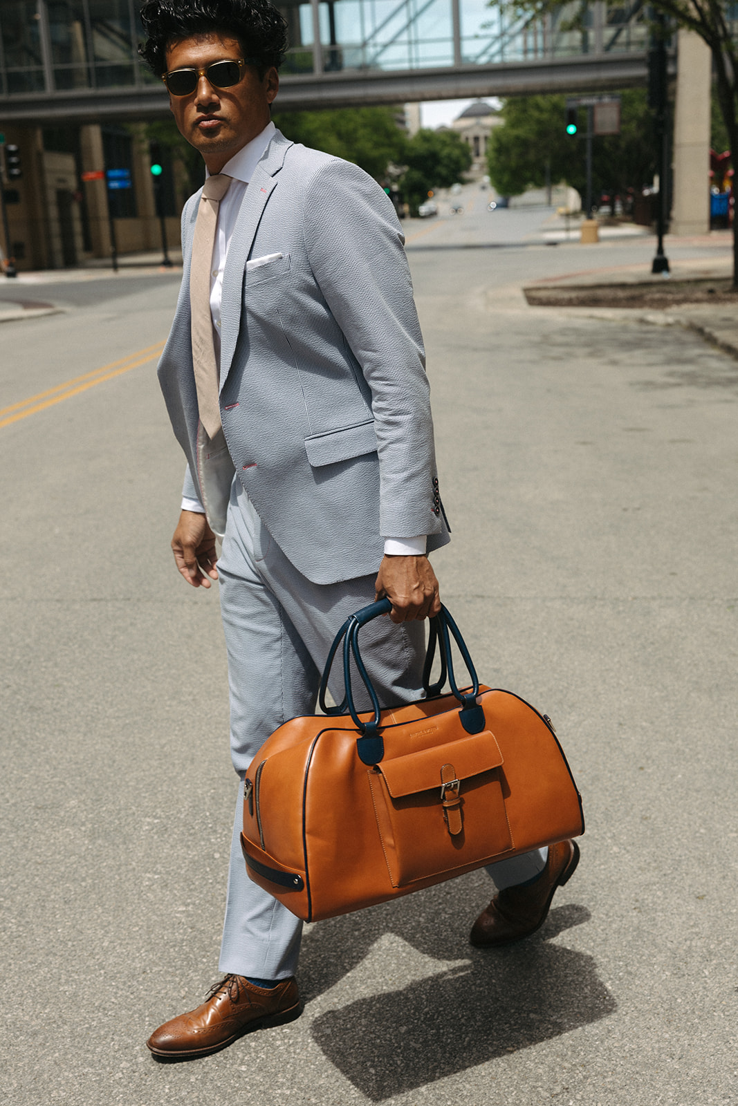 Man in a custom light grey suit carrying a leather duffel