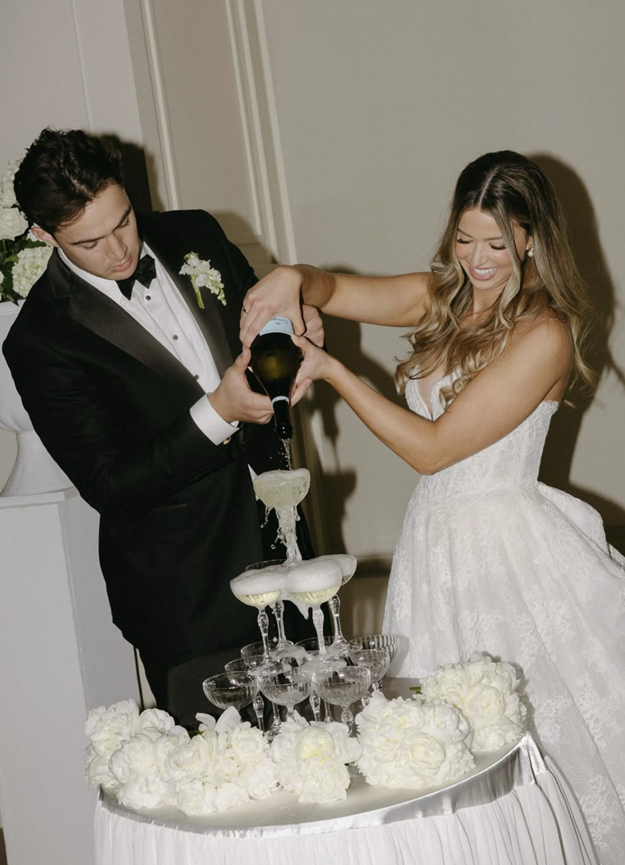 Groom in a custom tuxedo pouring a champagne tower with the bride